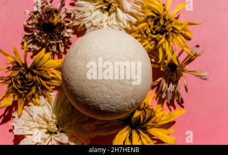 White bath bomb among the buds of dried flowers on a pink background.  Stock Photo