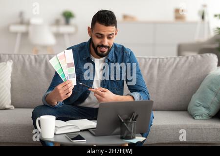 Arab guy showing color swatches at laptop screen at home office, presenting graphic design project on remote meeting Stock Photo