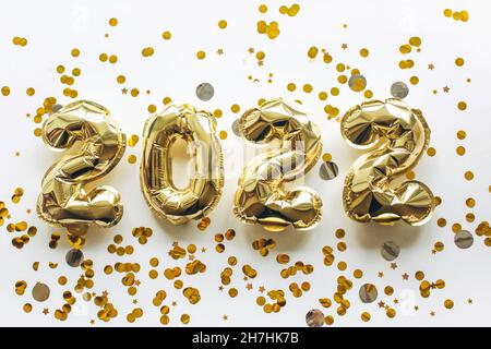 Balloons made of gold foil with the numbers 2022 on a white background with gold sequins. Celebrating Christmas, New Years and holiday concept. Flat lay, top view. Stock Photo