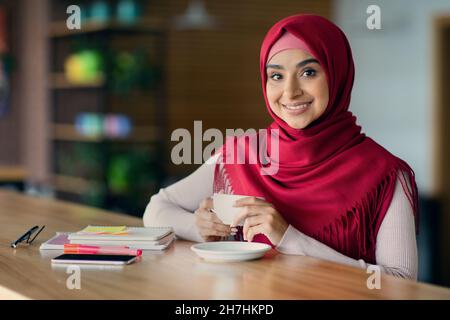 Portrait of smiling beautiful muslim woman drinking coffee at cafe Stock Photo