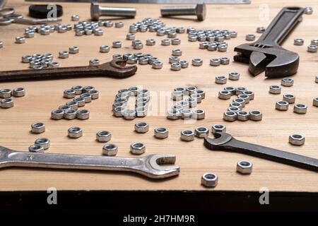 Number 2022 is lined with metal nuts on a wooden table next to a variety of wrenches and bolts. Concept of preparing for the New Year.  Stock Photo