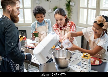 Group of happy children cooking together with cook in the kitchen, they learning to cook cake Stock Photo