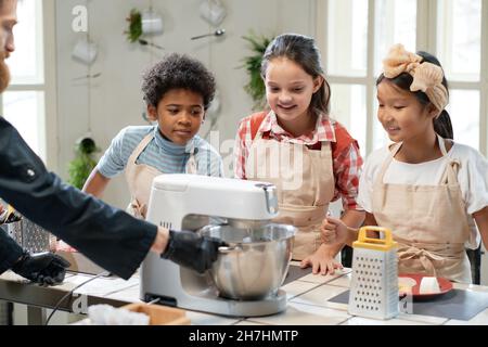 Cook making dough in mixer and teaching children to cook during his masterclass in the kitchen Stock Photo