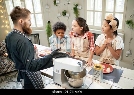 Children standing at the table and listening to the cook, they learning to cook together at the lesson Stock Photo