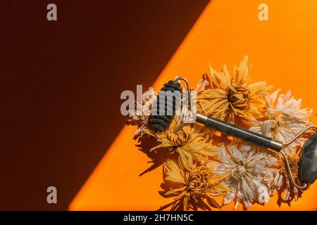 Green jade facial massager roller among dry buds on a yellow background. Stock Photo