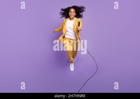 Photo of adorable pretty lady wear yellow suit glasses jumping holding microphone isolated purple color background Stock Photo