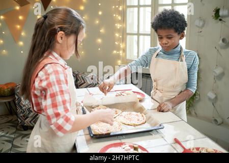 Children making pizza together at the table, they adding ingredients on the dough Stock Photo