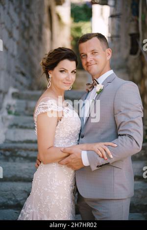 Groom holds the hand of bride while standing on the stone steps between the houses Stock Photo