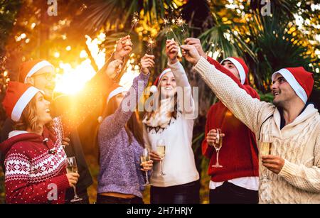 Young friends with santa hats celebrating Christmas with champagne wine toast outdoors - Tropical holidays concept with people group enjoying time Stock Photo