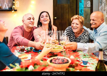 Mixed age group toasting white wine and having fun at winter holiday reunion - Dinner celebration concept with happy adult friends Stock Photo