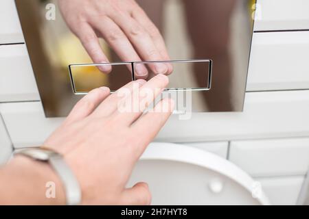 Hand presses a modern economical press for flushing clean water into the toilet, with two separate buttons.  Stock Photo