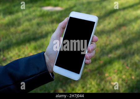 Mockup image of woman hand holding white mobile phone with blank black screen on the nature background. Stock Photo