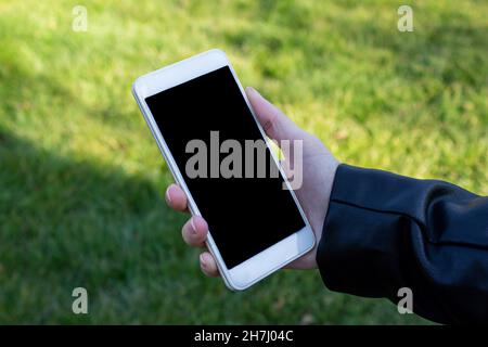 Mockup image of woman hand holding white mobile phone with blank black screen on the nature background. Stock Photo