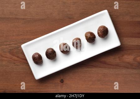 Long white plate with 6 roasted chestnuts on a wooden table Stock Photo