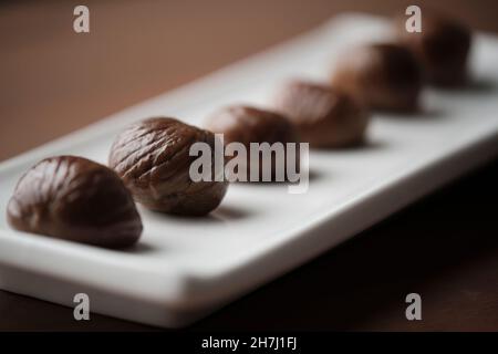 Long white plate with 6 roasted chestnuts on a wooden table Stock Photo