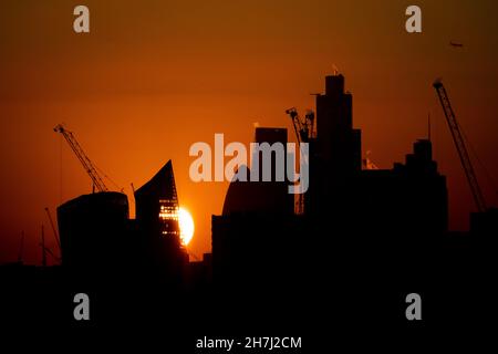 The sun sets behind construction cranes and the skyline of the financial district of London. Picture date: Tuesday November 23, 2021. Stock Photo