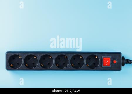 A black surge protector with portable sockets and a red button on a blue background. Free space Stock Photo