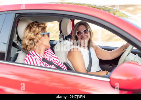 Two friends traveling in a rented red car, laughing and enjoying their vacation Stock Photo