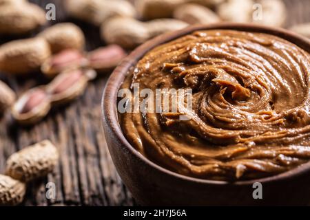 Peanut butter in wooden bowl and peanuts on rustic oak table. Stock Photo