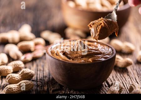 Peanut butter on spoon bowl and peanuts on wooden table. Stock Photo