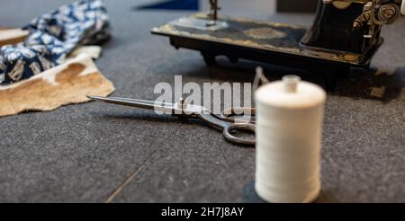 close-up of ancient and ruined seamstress scissors, in the background ancient sewing machine and fabrics, panorama Stock Photo