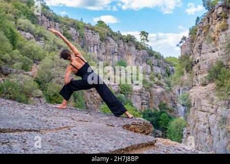 Unrecognizable woman doing parivritta parsvakonasana on rock Stock Photo