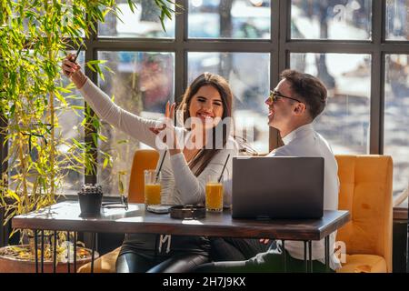 Beautiful young loving couple sitting in the cafe, having fun and taking a selfie. Stock Photo