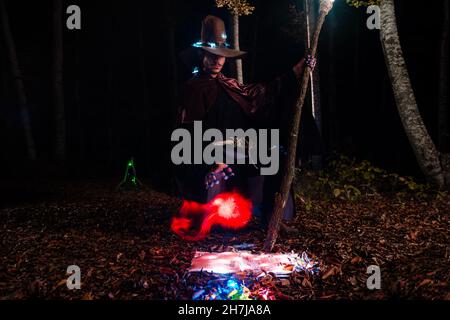 Wizard (mage) casting a spell with his magical staff while standing in an enchanted forest. Stock Photo