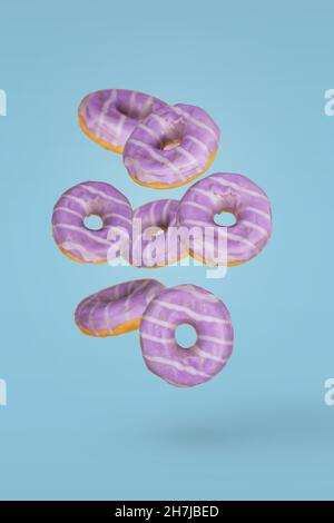Purple decorated doughnuts with blueberries in motion falling or flying on blue background. Minimal dessert and sweet concept Stock Photo