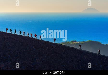Hikers walking around Gran Crater rim, Vulcano Island, Aeolian Islands, Sicily, Italy Stock Photo
