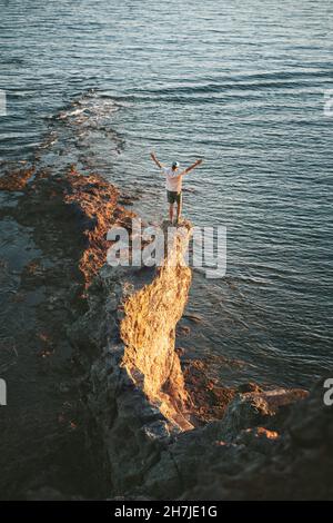 Man traveler standing on cliff edge rock above sea adventure travel lifestyle active vacations outdoor freedom concept Stock Photo