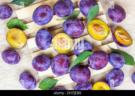 Top view of fresh raw blue and violet plums with green leaves on light wooden background. Stock Photo