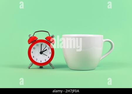 Alarm clock next to white tea cup on green backrgound Stock Photo