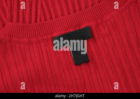 Close-up of a black label on a red sweater. Label on the back of the neckline of the sweater. Blank label on warm clothing. Stock Photo