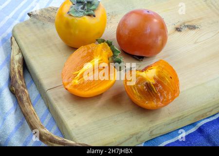 Fresh persimmon on a wooden board close-up. Persimmon of different varieties. Delicious healthy fruits in the fall. Ripe persimmon, cut in half. Stock Photo