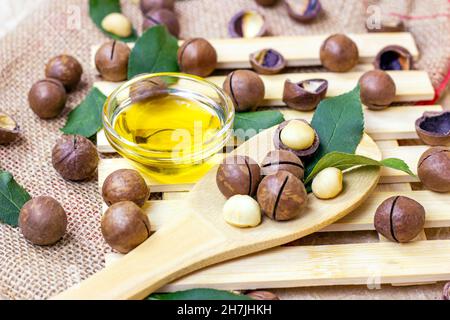 Brown macadamia nuts with yellow oil in a glass bowl on light wooden background. Stock Photo
