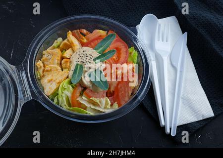 Salad with vegetables and chicken in a plastic container. Takeout food. Salad with cabbage, tomatoes and meat in a disposable bowl with disposable app Stock Photo