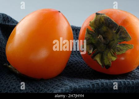 Orange ripe persimmon closeup. Two persimmons on a black kitchen towel. Ripe whole persimmon in autumn. Healthy orange berries. Stock Photo