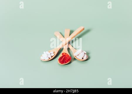 Various vitamins pills and capsules in wooden spoons on green background, close-up Stock Photo