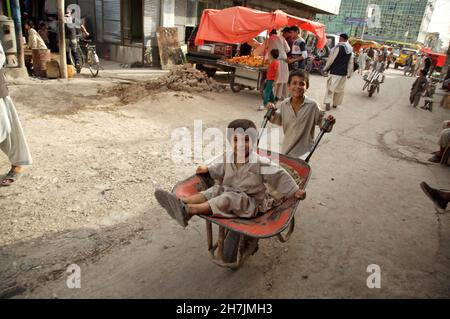 A young boy wheels his younger brother on a cart. They work as porter, at the main market, in the city of Mazar-e-Sharif, in the northern province of Stock Photo