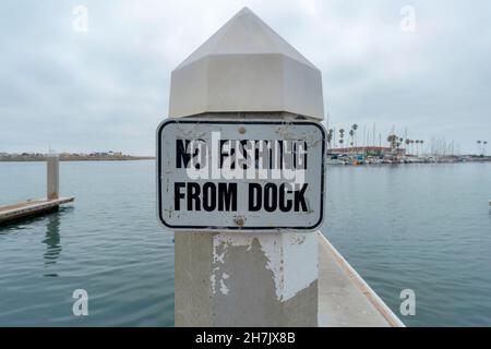No fishing from dock old signage at Oceanside, California. Close up of a signage on a post against the view of the water and harbor at the back. Stock Photo
