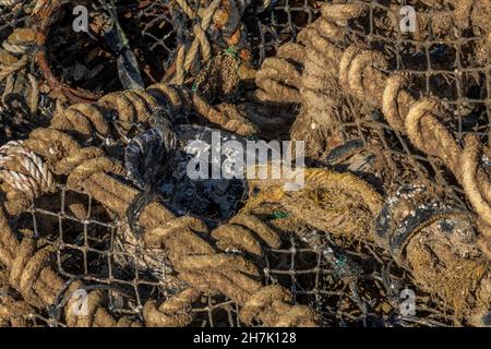 lobster pots left on the quayside to dry in the sun with tangled fishing equipment and old ropes. fishermans lobster potting kit on the harbour side. Stock Photo