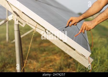 Close up of male hands checking voltage in solar panels with multimeter outdoors. Competente energy technician controlling work of solar station. Stock Photo