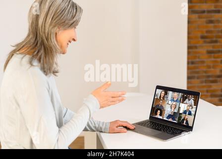 Senior female teacher using application for video communication with students online, holding webinar, classes. Mature tutor looking at laptop screen with people profiles and taling on distance Stock Photo