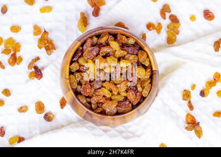 Top view of brown raisins (dried yellow grape) in round wooden bowl on light background. Stock Photo