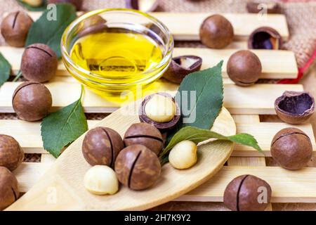Brown macadamia nuts with yellow oil in a glass bowl on light wooden background. Stock Photo