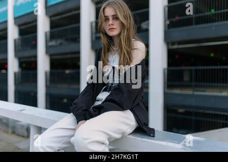The girl sits on the railing near the parking lot Stock Photo