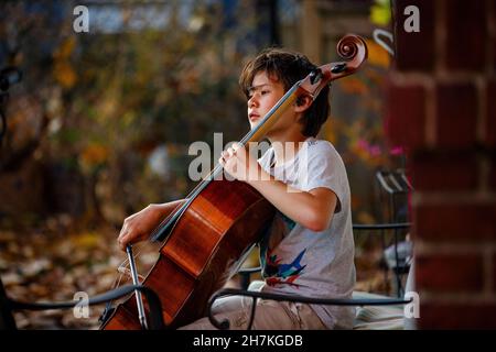 A focused boy plays cello outside in autumn Stock Photo