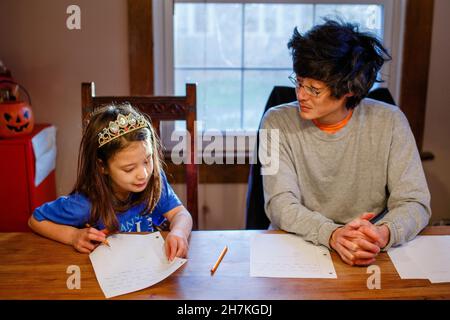 A little girl in princess crown does homework at table with father Stock Photo