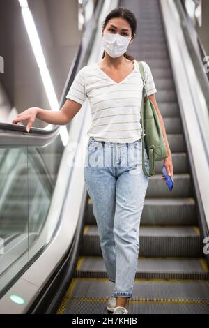 Woman in face mask going through escalator Stock Photo